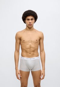 Γκρι βαμβακερά μπόξερ με λευκή ελαστική μέση που φέρει το λογότυπο «TOMMY HILFIGER» σε κόκκινο και μπλε χρώμα. Το μοντέλο στέκεται όρθιο, με απλό φόντο.