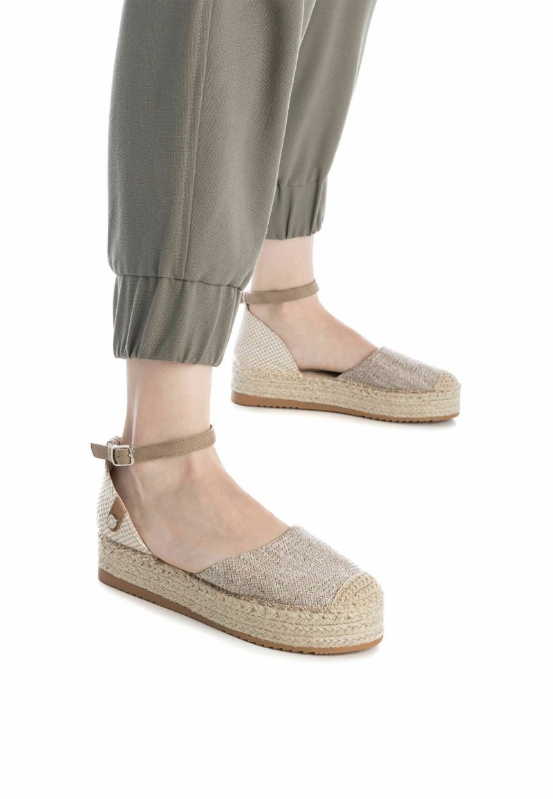 Alpargata con cuña, superior de tejido beige trenzado, tira de tobillo y suela envuelta en yute. Cuenta con un tacón bajo y una superficie texturizada.