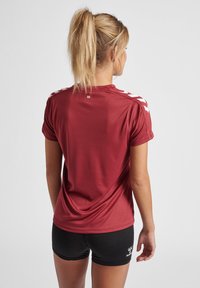 Rode sportshirt met korte mouwen, met witte accenten op de schouders. Gladde textuur, lichte stof geschikt voor sport.