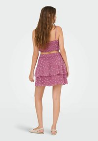 Completo a due pezzi composto da top corto e gonna a strati. Entrambi in un morbido rosa con motivi a diamante bianchi, realizzati in tessuto leggero.