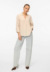 Blouse en lin beige avec un col en V, manches trois-quarts, coupe décontractée, associée à un jean large délavé et des escarpins à bout pointu.