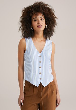 Chaleco sin mangas a rayas azul claro con un pronunciado escote en V, botones de madera y un dobladillo ligeramente curvado, combinado con pantalones marrones de corte holgado.