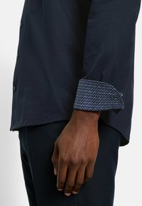 Marineblaue Hemdbluse mit einem gemusterten blauen Manschette. Glattes Material und moderne Passform, mit einem kontrastierenden Manschettendesign und strukturiertem Akzent.