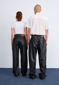 Zwarte leren broek met een hoge taille en een wijde pijp. Opvallend oranje label aan de achterkant. Beschikt over een gladde, glanzende textuur.