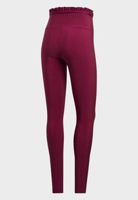 Höga mörkröda leggings med en volangkantad elastisk midja sedd bakifrån mot en enkel bakgrund.