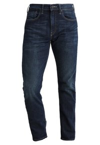 Vaqueros de mezclilla azul oscuro con corte recto, con sutiles efectos desgastados, cinco bolsillos y cierre de botón metálico.