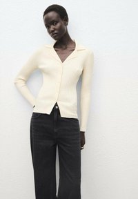 Crème ribgebreide cardigan met een kraag en knopen, gecombineerd met hoge taille zwarte jeans. Soepele textuur en een aansluitend ontwerp.