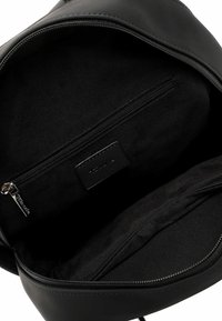 Interno dello zaino in pelle nera con un compartimento zip e un'etichetta. Texture liscia con un design semplice e funzionale.