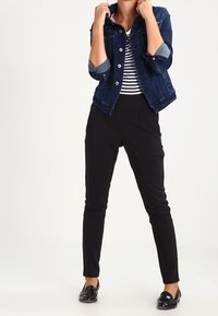 Džínová bunda v tmavě modré barvě s knoflíkovým zapínáním a ohrnutými rukávy, doplněná černými slim-fit kalhotami a černými mokasíny, s proužkovaným topem.