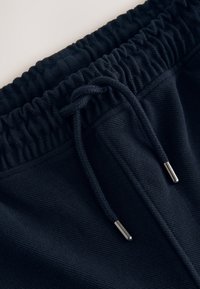 Nahaufnahme eines schwarzen elastischen Bündchens mit gebundenem Kordelzug und Metallendstücken an weichen Stoffhosen.