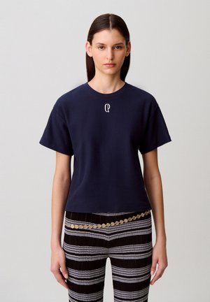 T-shirt blu navy a maniche corte in tessuto di cotone con scollo rotondo e piccolo logo bianco sul petto. Abbinata a pantaloni a righe bianche e nere.