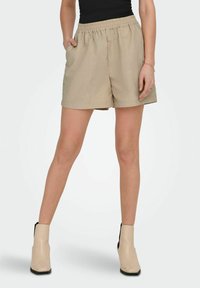 Beige shorts van lichtgewicht stof met een elastische tailleband, zijzakken en een relaxed fit, gecombineerd met beige enkellaarzen.