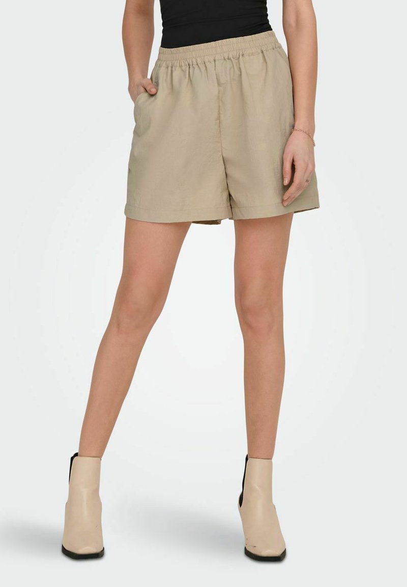 Beige shorts van lichtgewicht stof met een elastische tailleband, zijzakken en een relaxed fit, gecombineerd met beige enkellaarzen.
