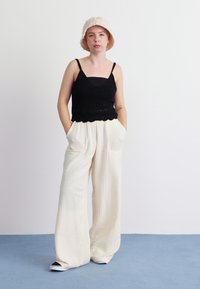 Black crochet tank top paired with cream wide-leg pants featuring a textured pattern, complemented by a light-colored bucket hat.