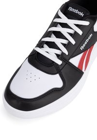 Mustad, valged ja punased Reebok tossud valgete paeltega, augulised varbad ja brändinimi keele ja külgpaneeli peal.