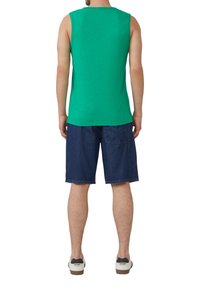 Grünes ärmelloses Tanktop mit Rundhalsausschnitt, kombiniert mit dunkelblauen Jeansshorts und lässigen Turnschuhen. Baumwollstoff, lockere Passform.