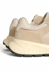 Zapatillas deportivas beige que combinan cuero liso y ante texturizado. La suela exterior es negra con una superficie estampada para mayor tracción.