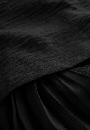 Svart tyg med en texturerad yta på toppen, lager med veckade draperier nedan, allt i varierande nyanser av svart.