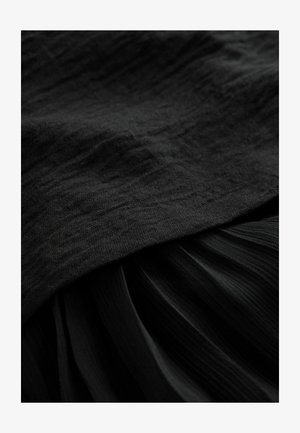 Svart tyg med en texturerad yta på toppen, lager med veckade draperier nedan, allt i varierande nyanser av svart.