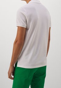 Bílá polokošile z měkké látky, s límečkem a krátkými rukávy, v kombinaci se zelenými šortkami.