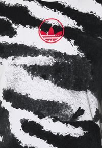 Svart och vit grafisk t-shirt med ett strukturerat vågmönster, med en röd broderad Adidas-logotyp centralt placerad.