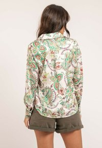 Chemise à manches longues en tissu crème ornée d'un motif paisley coloré avec des accents verts, rouges et roses, associée à un short gris.
