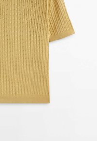 Żółty sweter w krótkim rękawie, dziany z teksturowanym wzorem w warkocz, z prążkowanym dołem i rękawami, wykonany z miękkiego materiału.