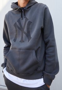 Sweat à capuche gris en polaire avec un grand logo sombre sur la poitrine, capuche à cordon, poche kangourou, poignets et ourlet côtelés.