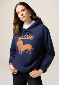 Granatowy hoodie z sznurkiem, z teksturowanym pomarańczowym wzorem psa i napisem "PARIS DOG" w pogrubionej czcionce. Gładki materiał i luźny krój.