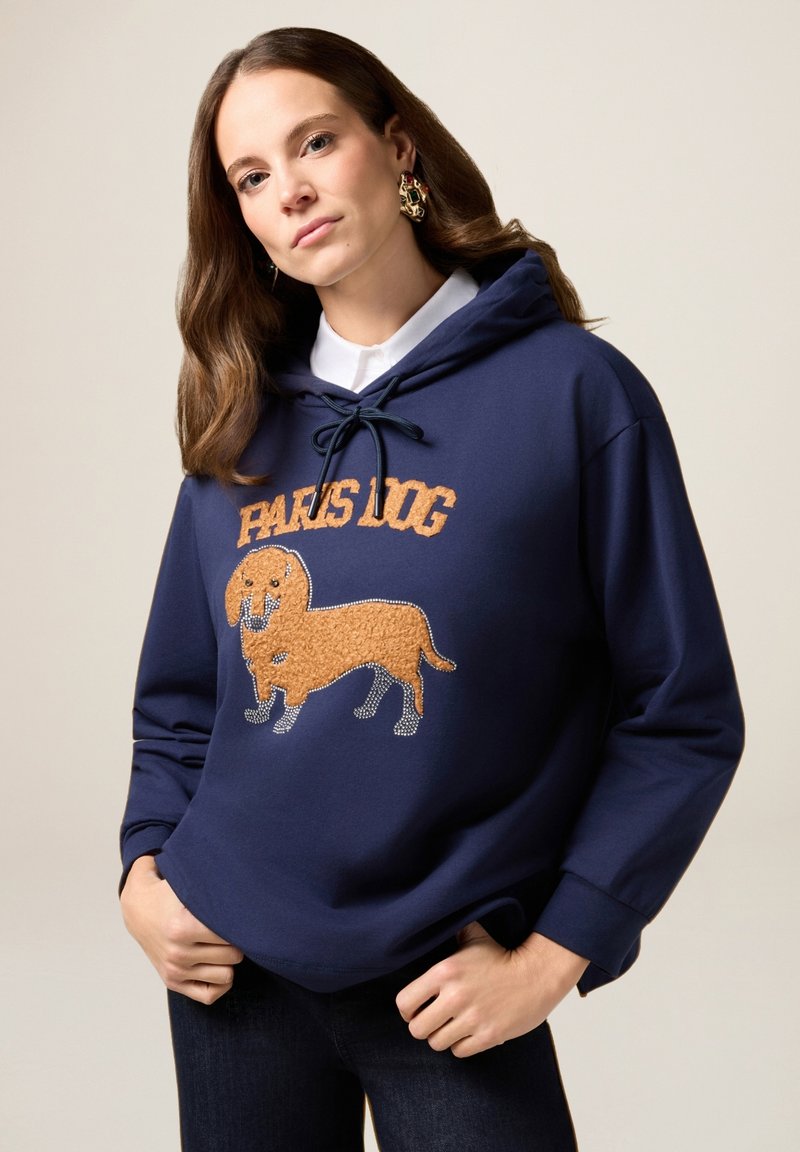 Granatowy hoodie z sznurkiem, z teksturowanym pomarańczowym wzorem psa i napisem "PARIS DOG" w pogrubionej czcionce. Gładki materiał i luźny krój.