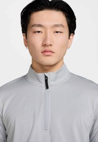 Világosszürke, negyedcipzáros pulóver texturált felülettel, fekete cipzáras záródással és álló gallérral.