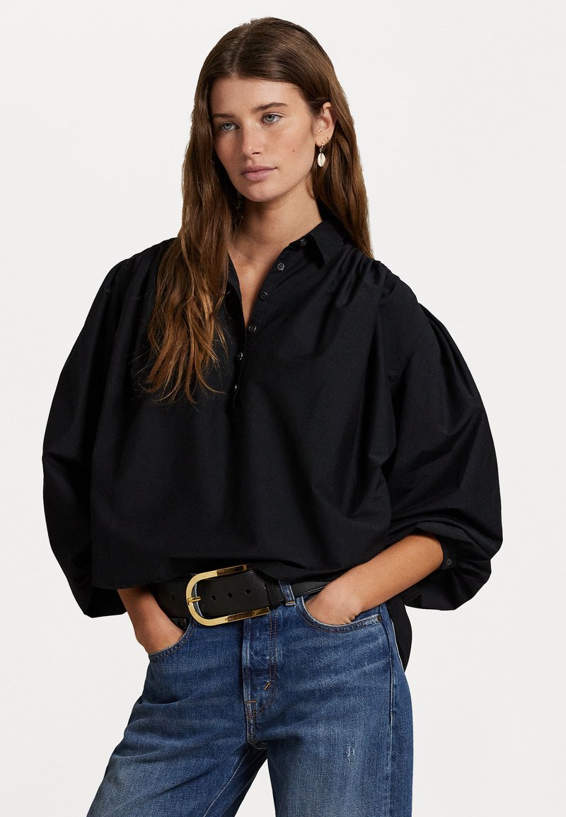Svart oversized knapper skjorte med krage og samlede ermer, båret med blå denimjeans og et svart belte med gullhardware.