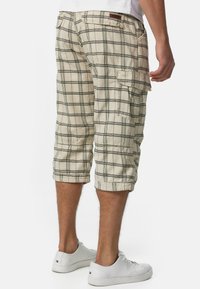 Shorts cargo beiges avec un motif à carreaux vert et noir, de longueur genou, dotés de poches latérales et de bords roulés. Le matériau semble léger.