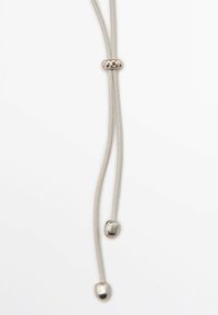 Corda in pelle con accenti in metallo color argento, caratterizzata da una perla centrale e due estremità rastremate. La corda è liscia e di colore chiaro.