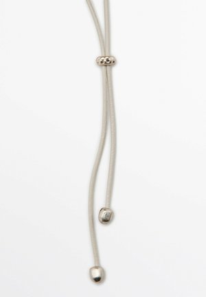 Sznur skórzany z metalowymi, srebrzystymi ozdobami, z centralną koralikiem i dwoma zwężającymi się końcami. Sznur jest gładki i jasnokolorowy.