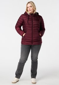 Doudoune bourgogne avec capuche, dotée d'une fermeture éclair et de poches latérales, associée à un jean gris et des sneakers blanches.