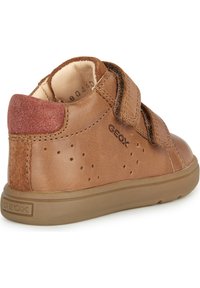 Zapatilla de cuero marrón con talón de ante, tira de Velcro, lados perforados para transpirabilidad y suela de goma. Logo de la marca mostrado en el costado.