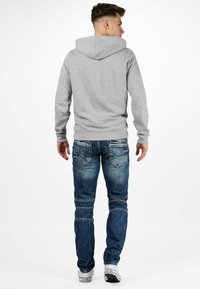 Un sweat à capuche gris avec une grande capuche, des poignets et un ourlet côtelés. Assorti à un jean en denim bleu avec une finition décolorée et plusieurs poches.