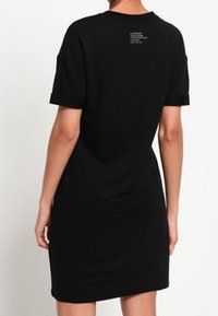 Robe t-shirt noire à manches courtes en doux tissu, légèrement ample, avec un col rond et une impression minimaliste au dos.