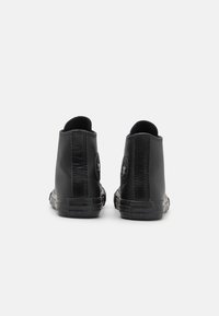 Schwarze High-Top-Sneaker aus glattem Material, mit einer strukturierten Sohle und runder Logo auf der Seite. Verfügt über flache Schnürsenkel und Knöchelschutz.