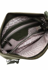 Olive green textured bag interior with a zippered pocket, lined with light pink fabric featuring repeating text patterns. Metal hardware visible.