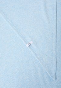 Tejido de algodón azul claro con una textura suave, con un diseño triangular y una etiqueta blanca cosida con "CECI" en texto negro.
