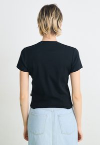 Schwarzes T-Shirt mit kurzen Ärmeln und Rundhalsausschnitt, aus weicher Baumwolle, taillierte Passform, minimalistischer Stil und gesäumter Saum.