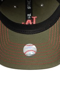 Olivgrüne Baseballmütze mit schwarzem Schirm. Verfügt über rote Nähte und ein rundes MLB-Label mit Baseballgrafiken und Text.