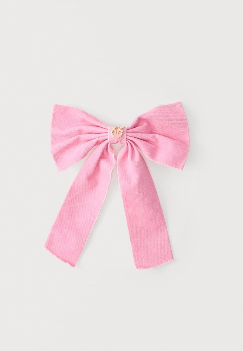 Ροζ υφασμάτινο φιόγκος με δύο μακριές ουρές και ένα μικρό χρυσό μενταγιόν στέμματος στο κέντρο, παρουσιασμένο σε απλό ανοιχτό φόντο.