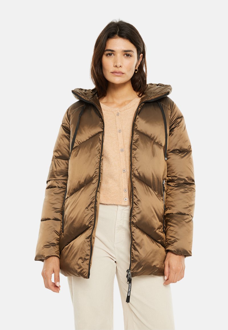 Chaqueta acolchada marrón con capucha, con patrones de rombos acolchados, cremalleras negras de contraste y bolsillos laterales. Llevada sobre un suéter ligero.