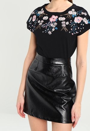 Black T-shirt with floral embroidered design in pink and blue, paired with a shiny black faux leather mini skirt, featuring a high waist.