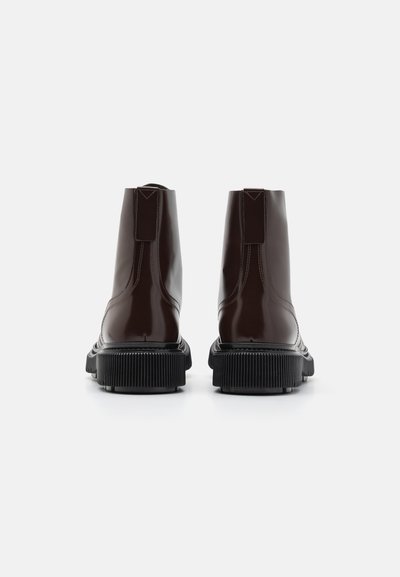 Bottines brunes brillantes avec un design épuré, semelles en caoutchouc noir texturé et accents de couture verticale à l'arrière.