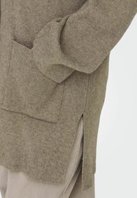 Cardigan vert olive avec texture côtelée, fente sur le côté et poche avant. Tissu en maille douce. Semble avoir une coupe décontractée avec des manches longues.