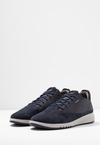 Sneakers blu navy con una combinazione di suede e pelle perforata, dotati di una suola grigia chiara e lacci blu. Design semplice e sportivo.